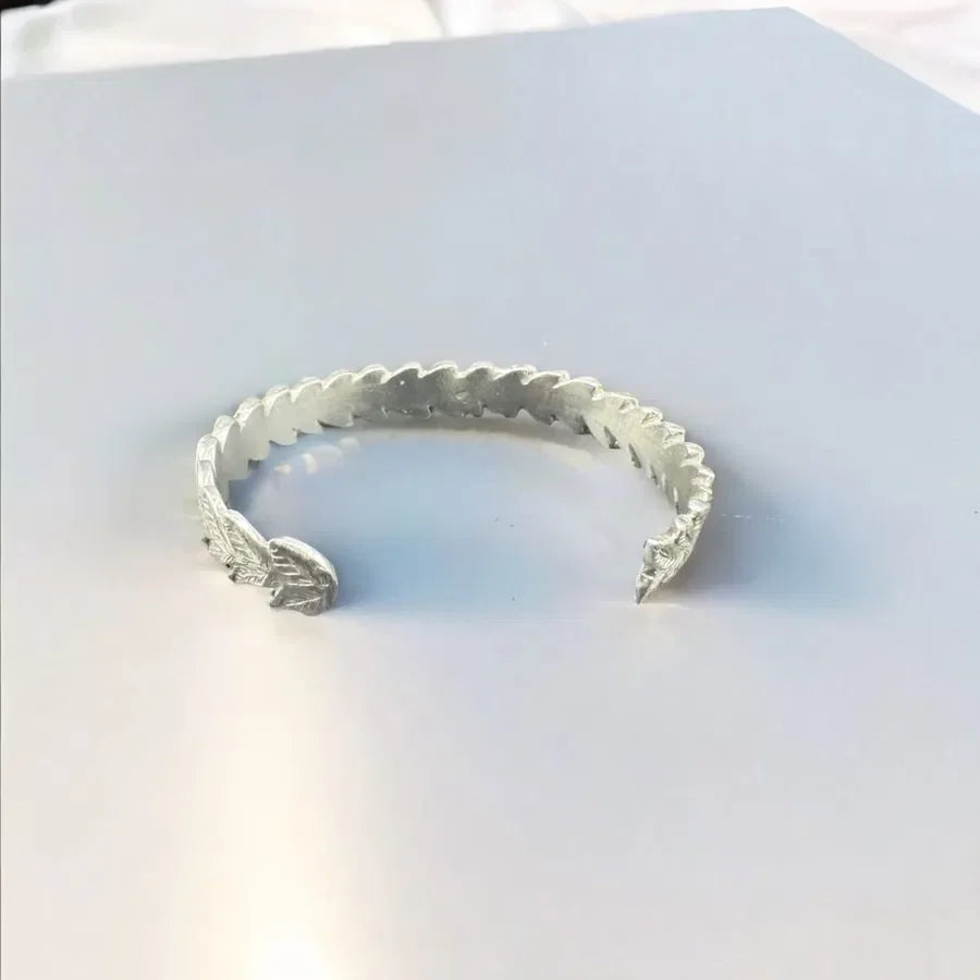 Handcrafted silver cuff bracelet with textured, leaf-inspired sculptural design on white background