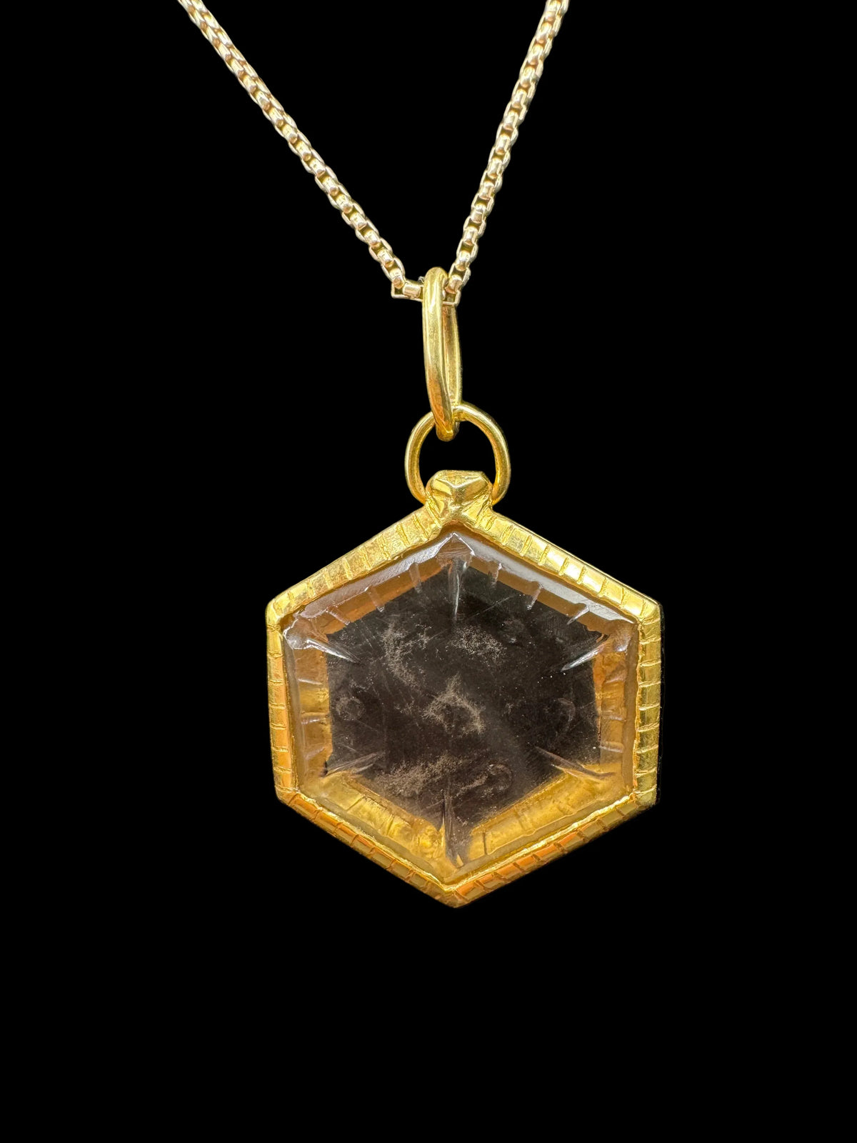 Handcrafted hexagon gold pendant necklace with dark gemstone on black background