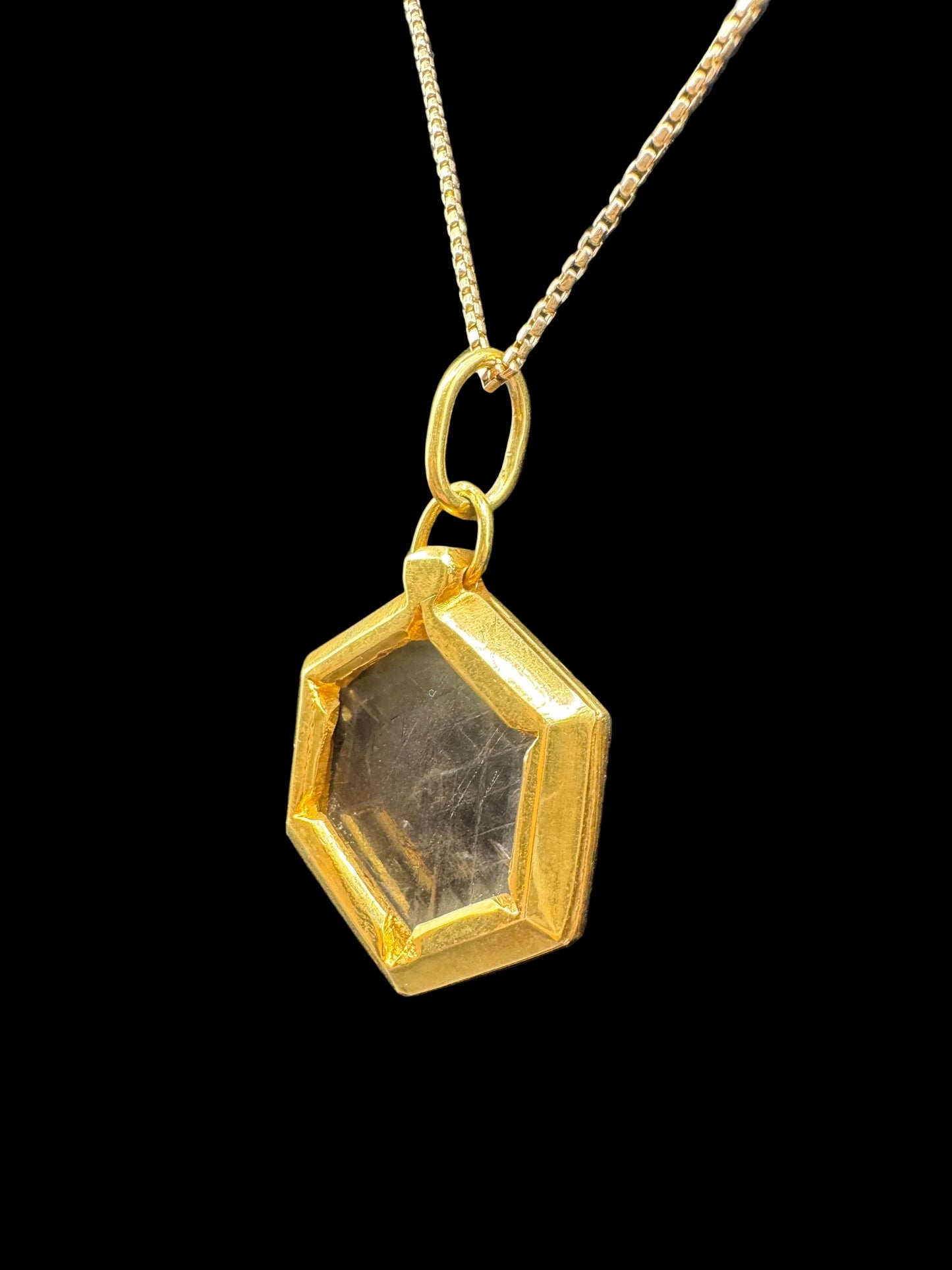 Gold hexagon pendant necklace with clear gemstone on gold chain, black background