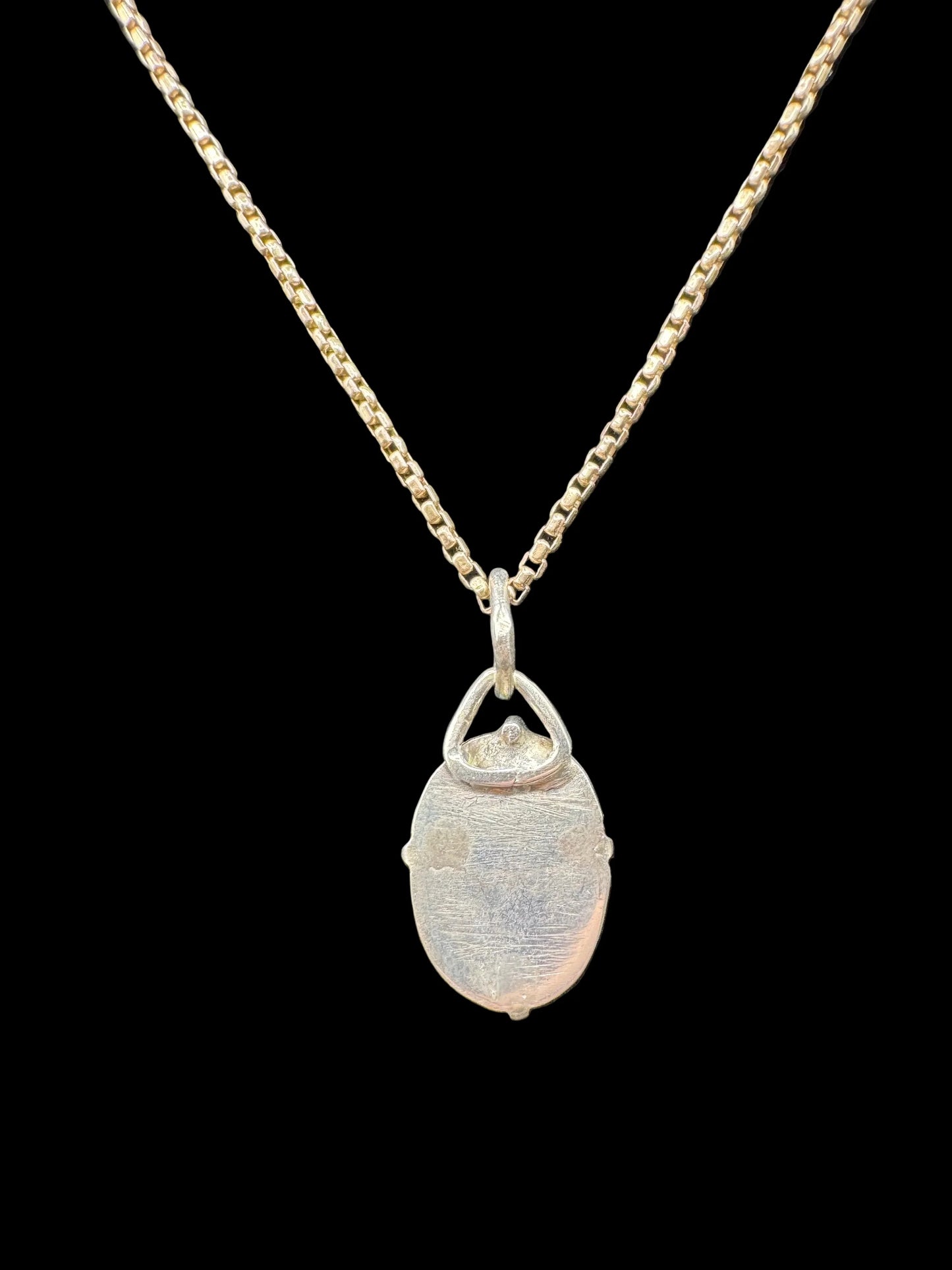 Handcrafted silver oval pendant necklace with textured finish on a gold chain, black background