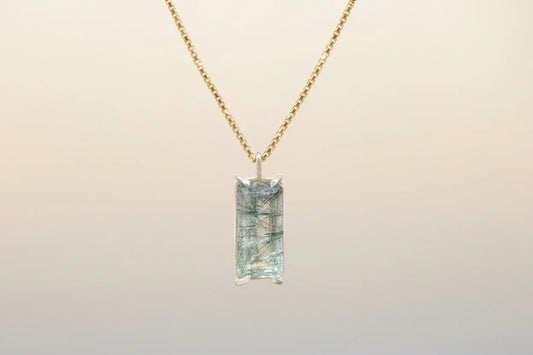 Gold chain necklace with rectangular rutilated quartz pendant on neutral background