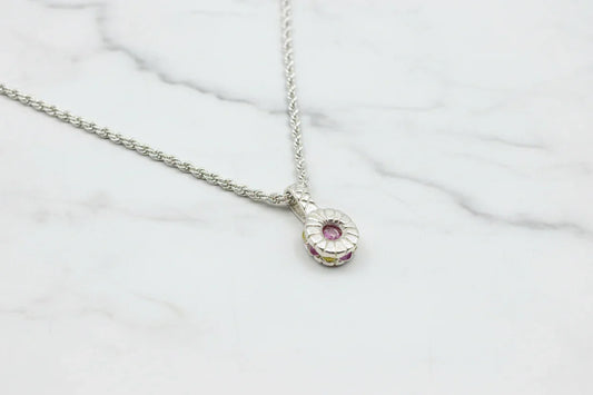 Handcrafted silver necklace with round pink gemstone pendant on marble background