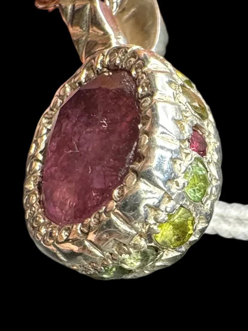 Handcrafted pendant with textured silver, large pink stone, and small green gemstone accents