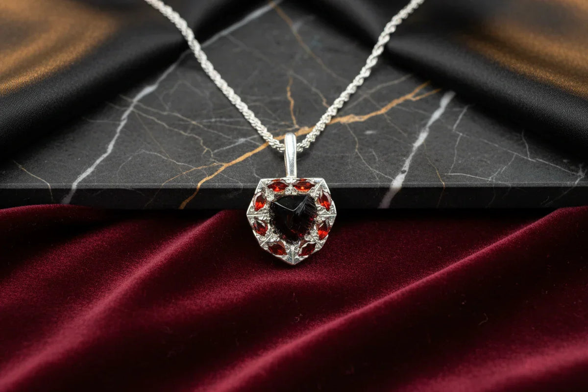 Handcrafted silver necklace with a red gemstone pendant on marble and velvet background