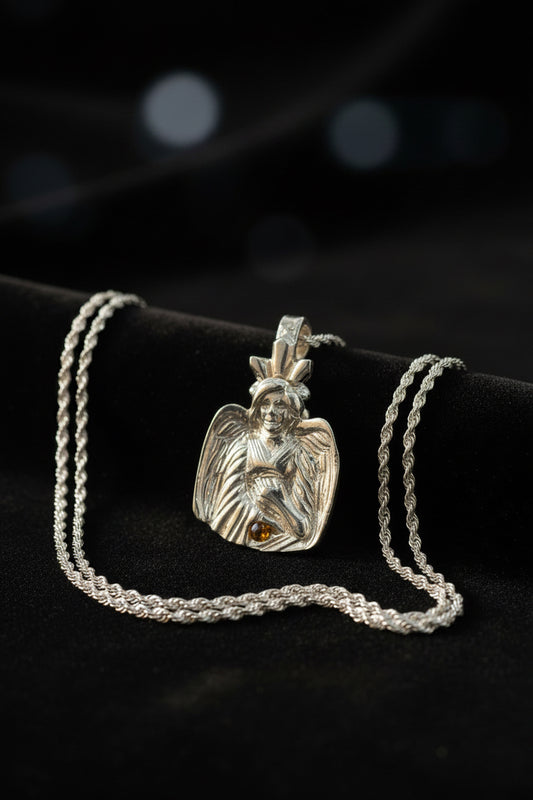 A silver angel pendant necklace with a detailed winged figure and a small amber gemstone, displayed on a black velvet surface with a silver chain.