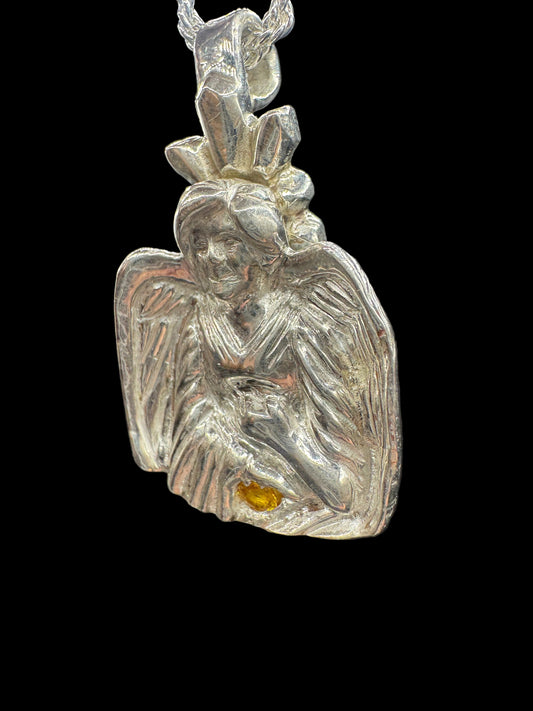 A silver-toned metal pendant or charm with a textured, organic leaf-like or wing-like shape, featuring a small amber-yellow inset detail, shown against a dark background.