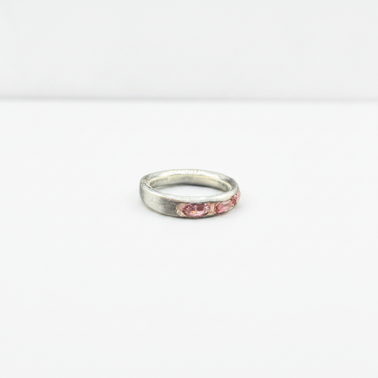 A silver band ring with a row of small pink gemstones set along the front, photographed on a plain white background.