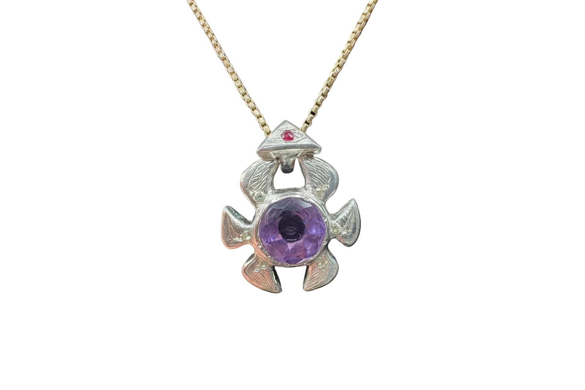 Silver pendant with purple gemstone and red stone on a gold chain against a dark background