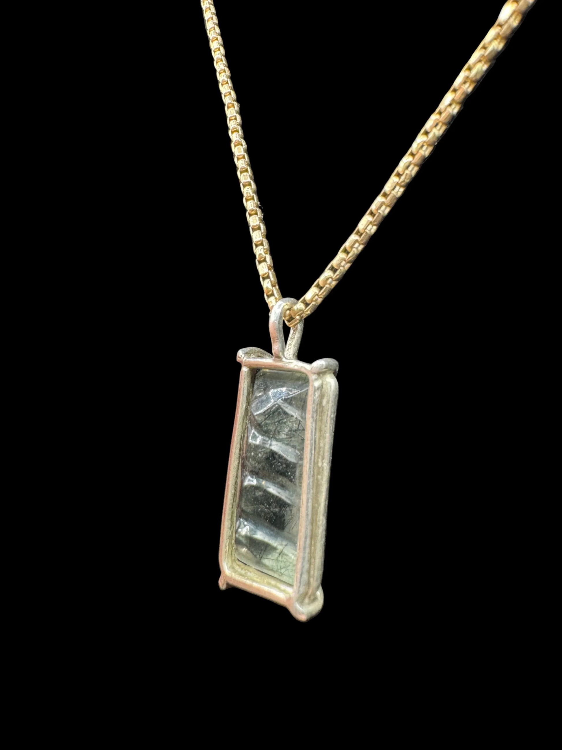 Handcrafted gold chain necklace with a rectangular crystal pendant on black background