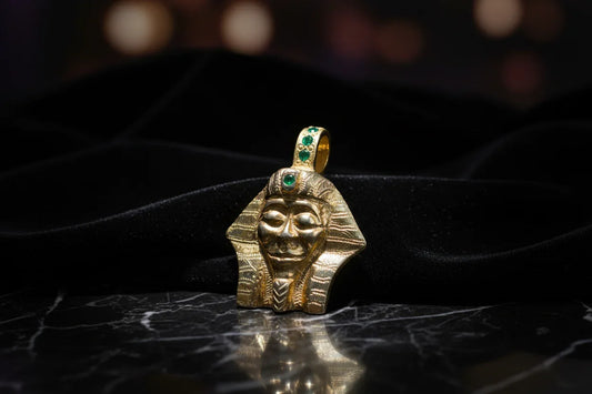 Handcrafted gold pharaoh pendant with green gemstones on black velvet background