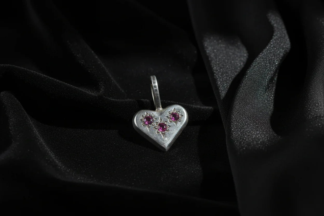 Handcrafted silver heart pendant with three purple gemstones on black fabric