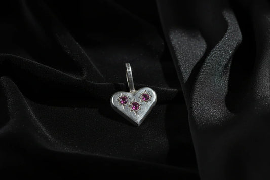 Handcrafted silver heart pendant with three purple gemstones on black fabric