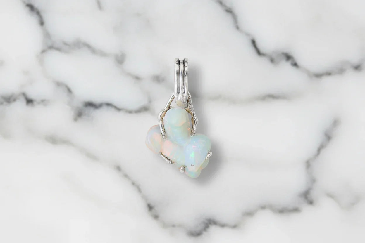 Handcrafted opal gemstone pendant with silver setting on white marble background