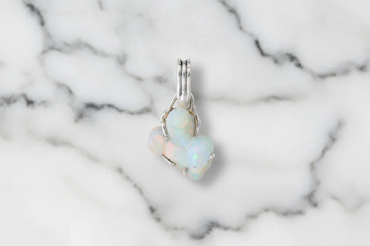 Handcrafted opal gemstone pendant with silver setting on white marble background
