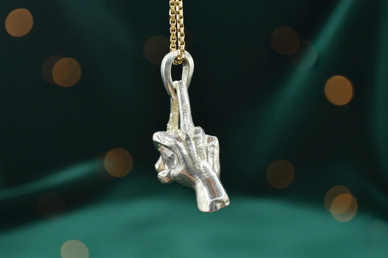 Handcrafted silver hand pendant necklace with gemstone detail on a gold chain, green backdrop