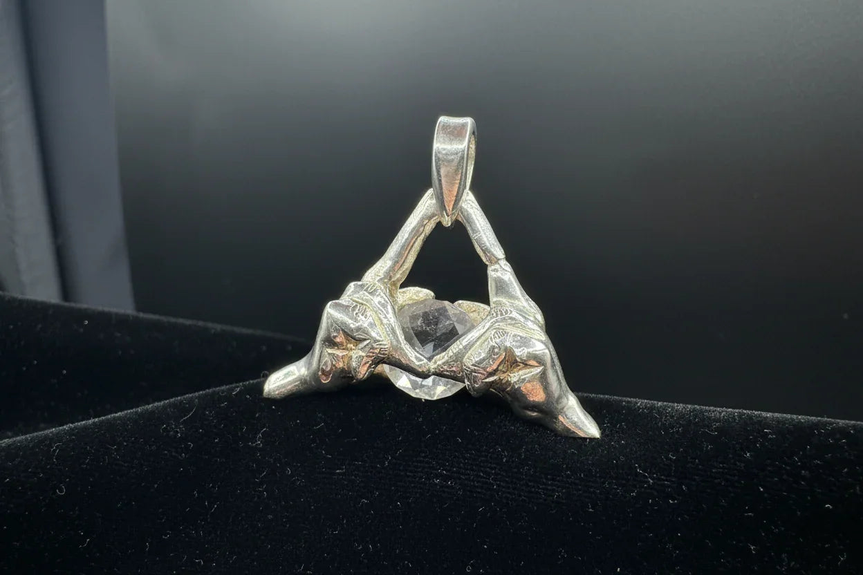 Handcrafted silver pendant with sculpted hands forming a triangle, featuring a clear gemstone