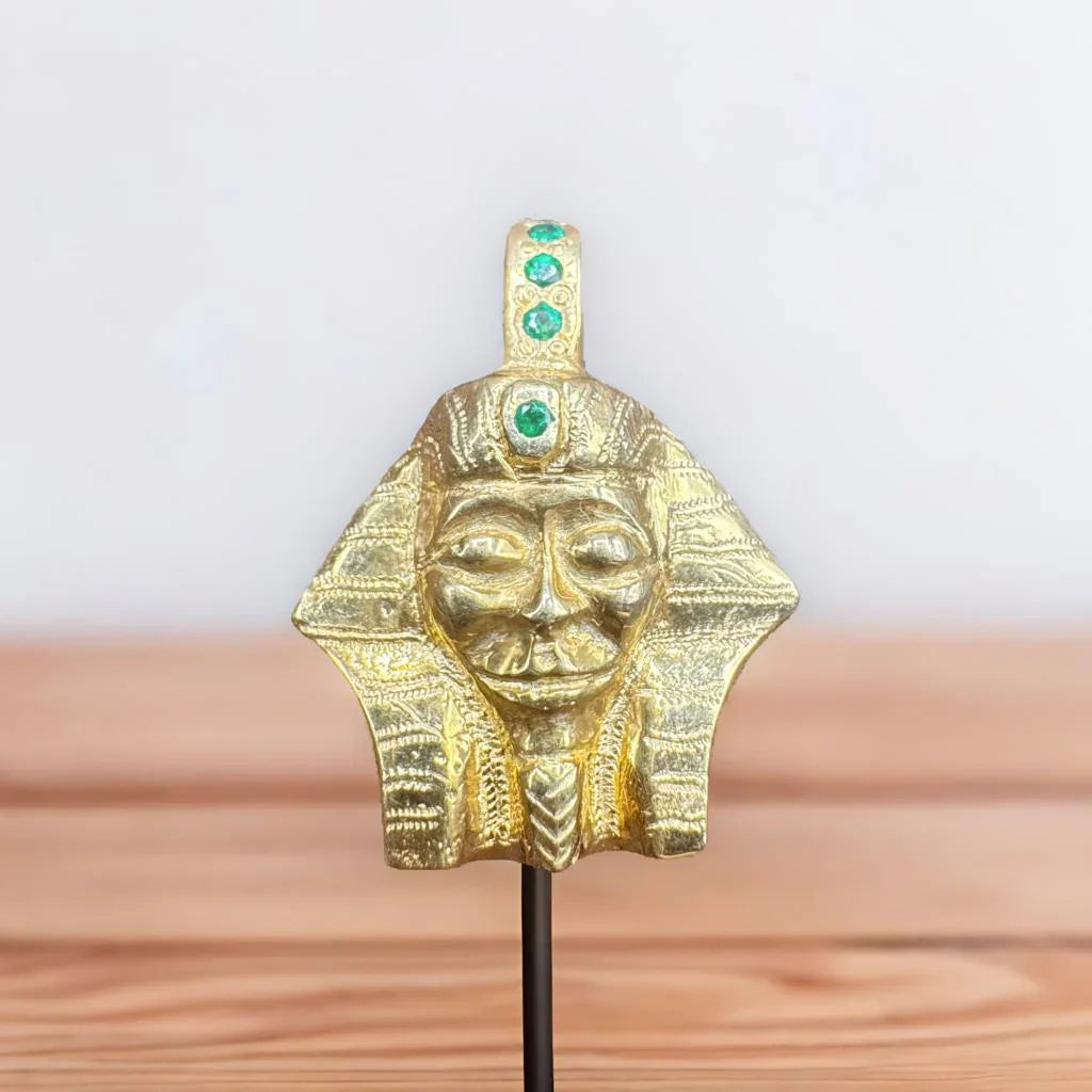 Handcrafted gold pharaoh pendant with green gemstone accents on a wooden surface
