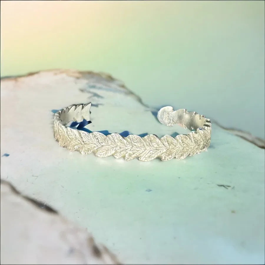 Handcrafted silver cuff bracelet with textured leaf pattern on a pastel background