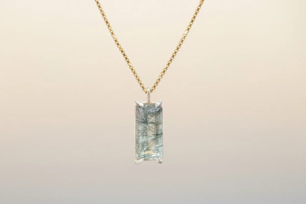 Gold chain necklace with rectangular rutilated quartz pendant on neutral background