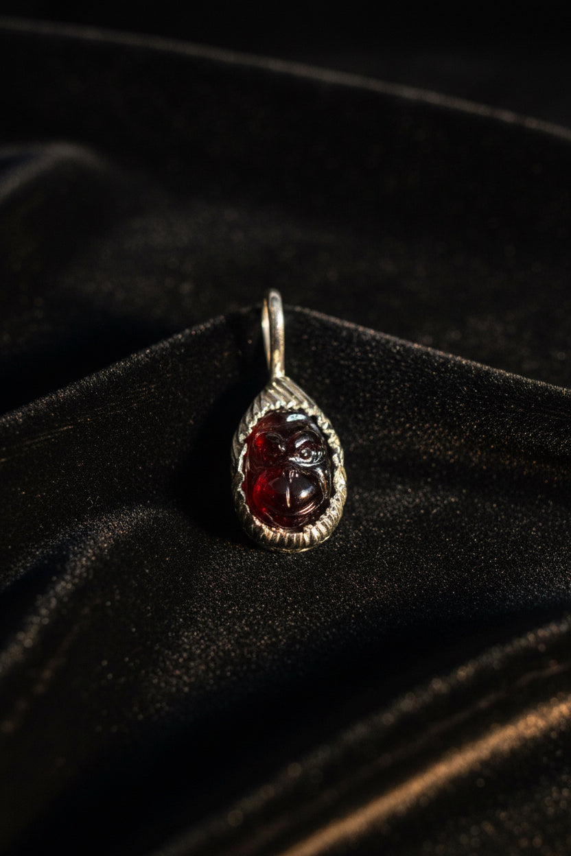 A teardrop-shaped silver pendant featuring a carved dark red gemstone, resting on a textured black velvet surface.