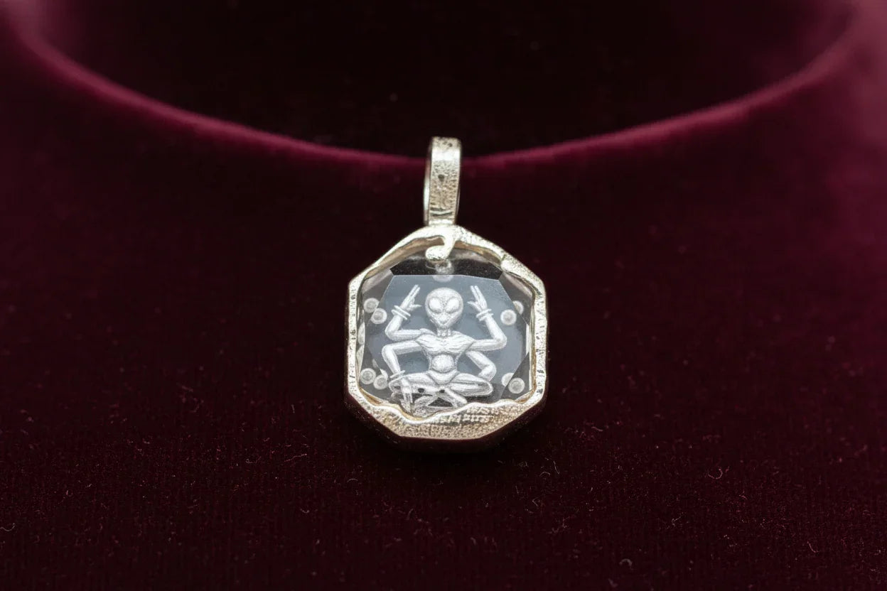 Handcrafted silver pendant with engraved alien figure on faceted clear gemstone, velvet background