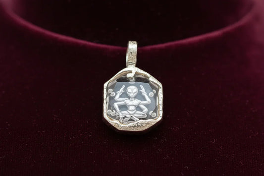 Handcrafted silver pendant with engraved alien figure on faceted clear gemstone, velvet background