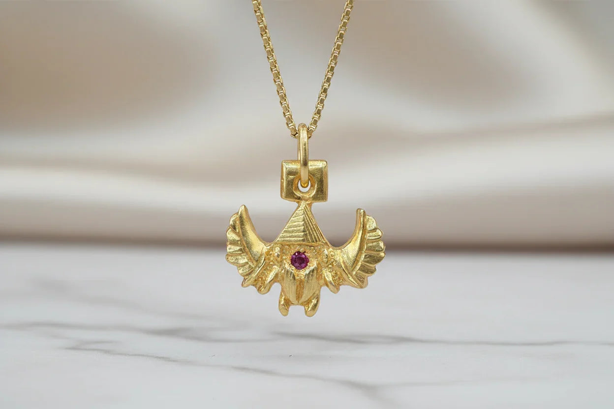 Gold handcrafted bird pendant necklace with red gemstone on marble surface