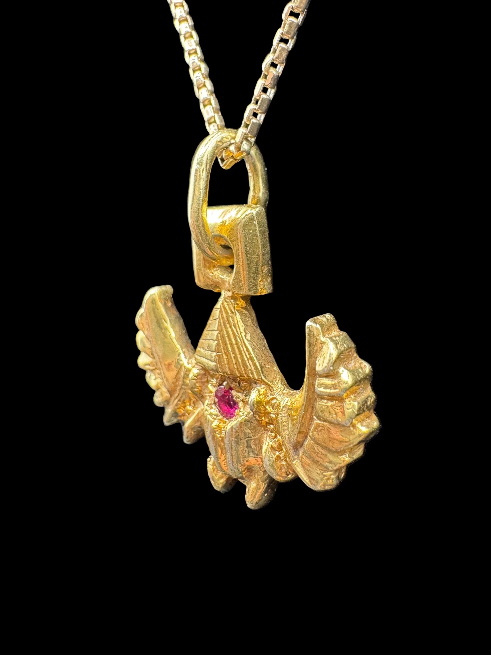 Handcrafted gold pendant with a red gemstone on a chain, sculpted in a unique abstract style.