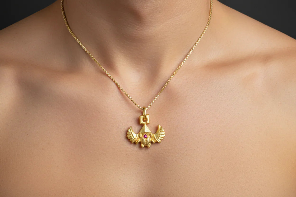 Gold handcrafted bird pendant necklace with red gemstone on model's neck