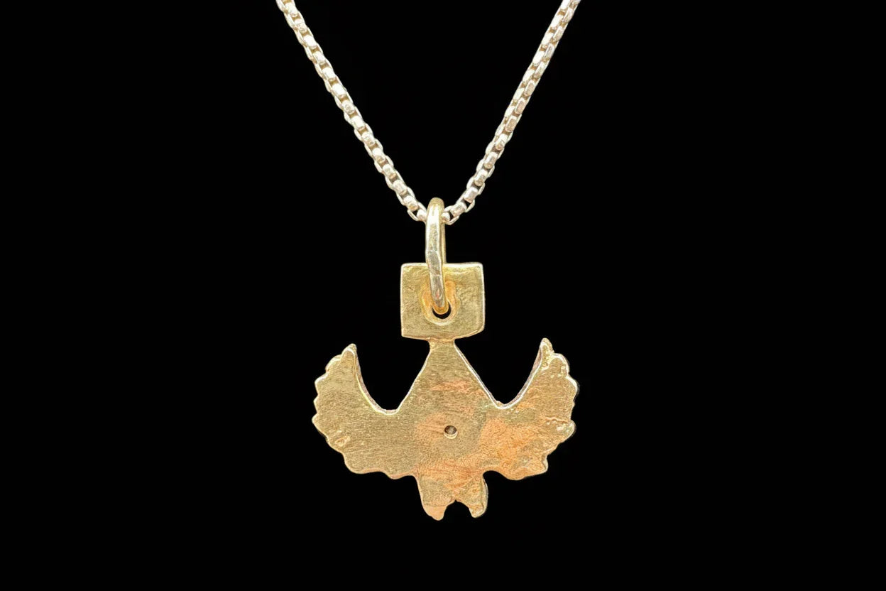 Handcrafted gold bird pendant necklace on a silver chain, artisan jewelry on black background
