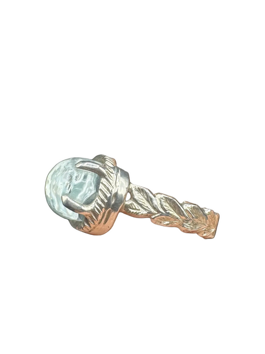 Silver ring with a clear gemstone on a finger against a dark background