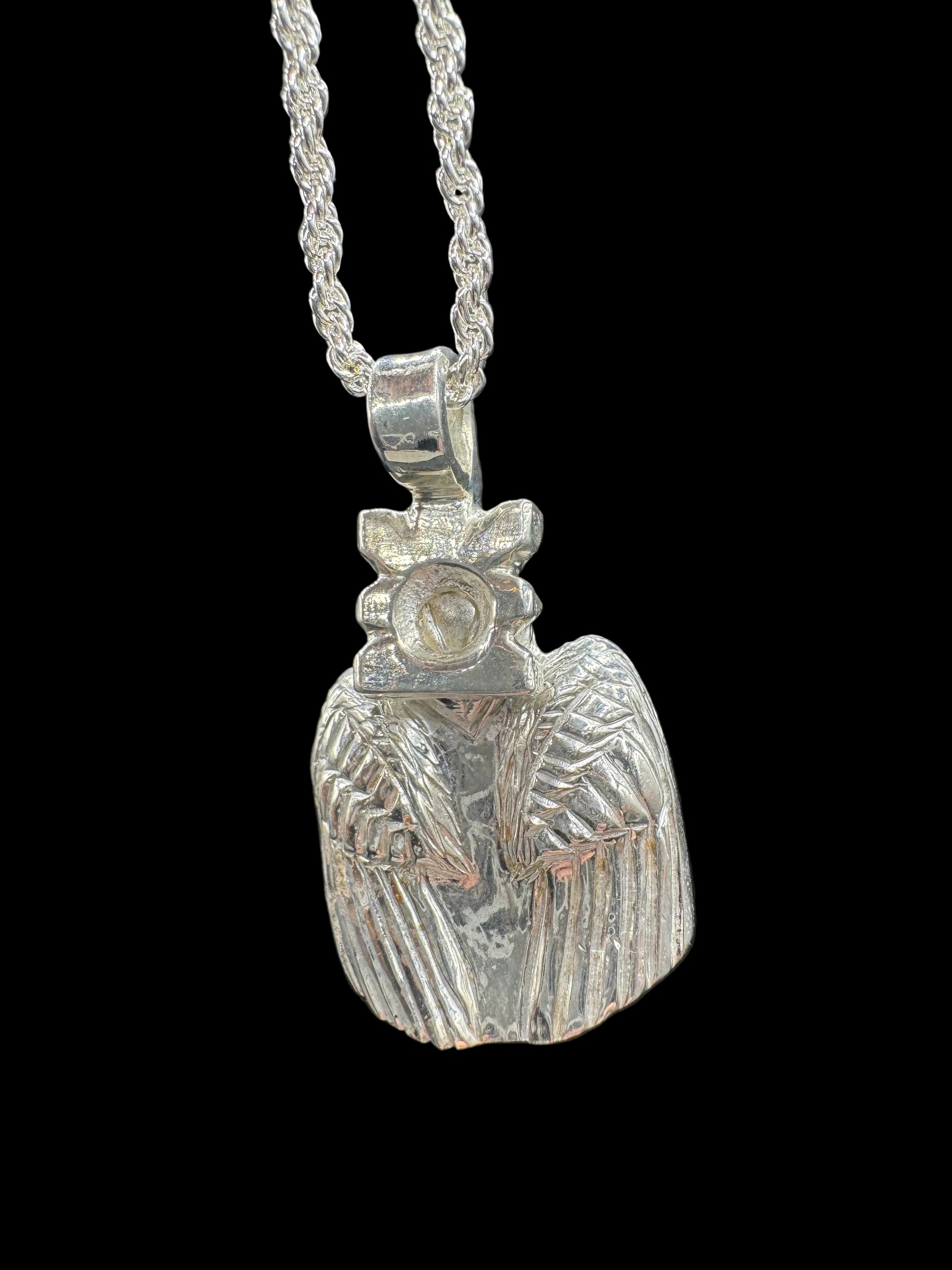 A silver pendant necklace featuring a carved, textured bird design, shown against a dark gray background.