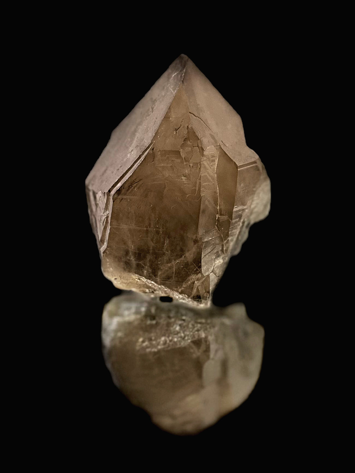 A raw, natural smoky quartz crystal point with visible internal inclusions, displayed on a reflective black surface against a solid black background.
