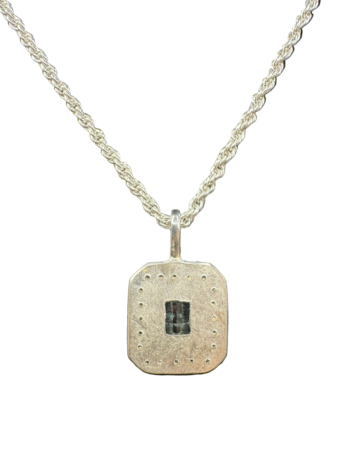 A silver-toned pendant necklace featuring a textured, octagonal tag-style pendant with a small dark rectangular inlay in the center, suspended from a twisted chain against a black background.