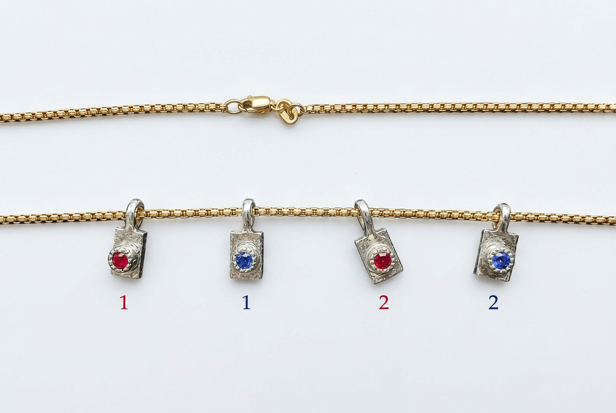 A gold chain necklace displayed on a white background, with four small pendant charms hanging below. Two pendants are silver-toned with a red gemstone, and two are silver-toned with a blue gemstone.