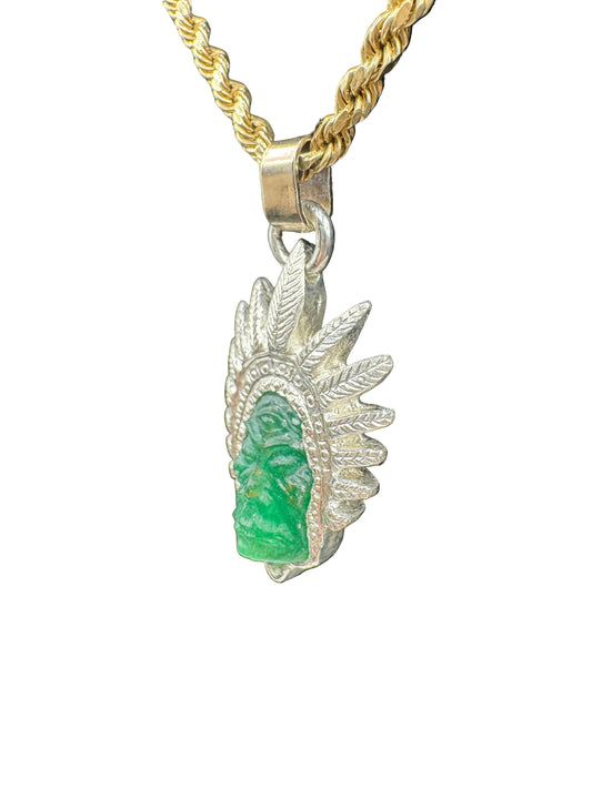 A gold and silver pendant necklace featuring a carved green stone face set against a feathered headdress design, suspended from a twisted gold chain on a white background.