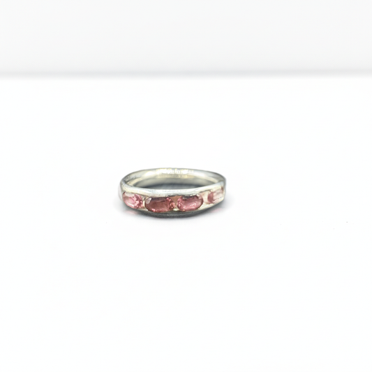 A silver band ring featuring a row of small pink gemstones, photographed on a plain white background.