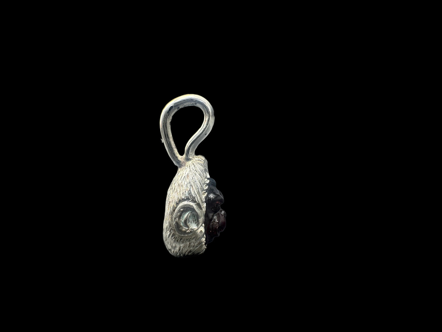 A small silver pendant with a textured, organic shape and a dark, polished stone inset, shown against a solid black background.