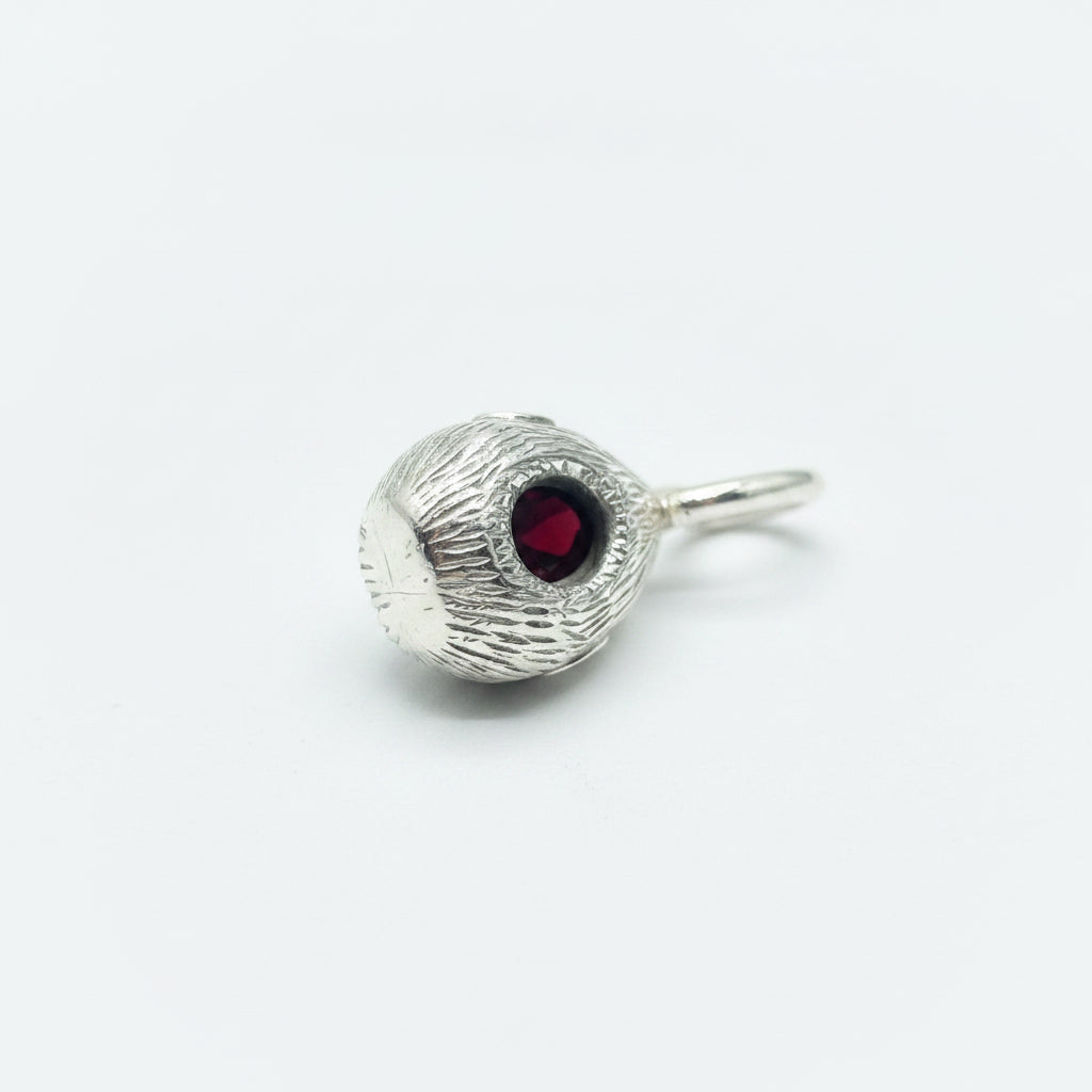 A silver-toned textured bead charm with a central round red gemstone, shown on a plain white background.