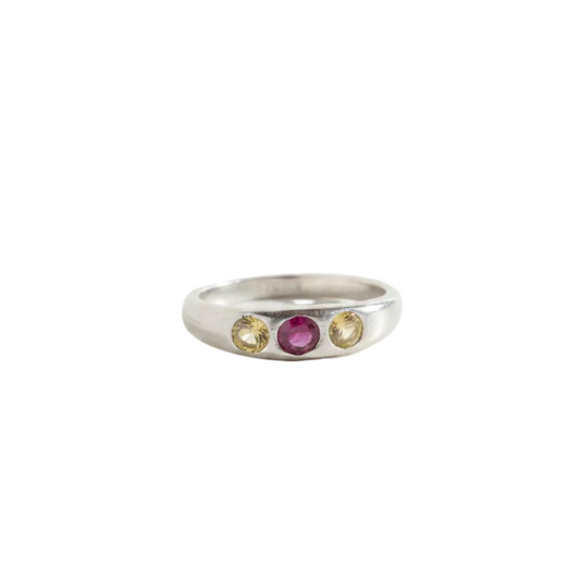 A silver band ring featuring three small round gemstones set in a row: a central pinkish-purple stone flanked by two pale yellow stones, shown on a plain white background.