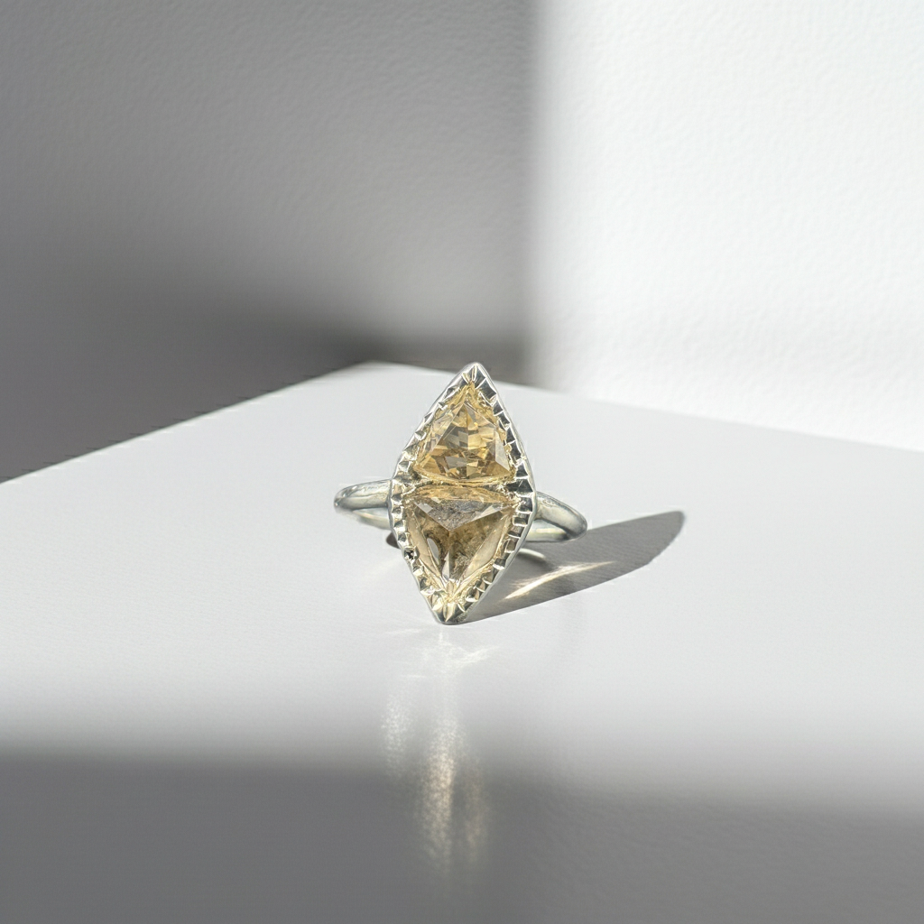 A silver ring featuring a marquise-cut yellow gemstone in a decorative bezel setting, displayed on a white surface with dramatic side lighting and a soft reflection.