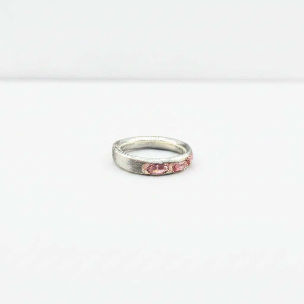A silver band ring with a row of small pink gemstones set along the front, photographed on a plain white background.
